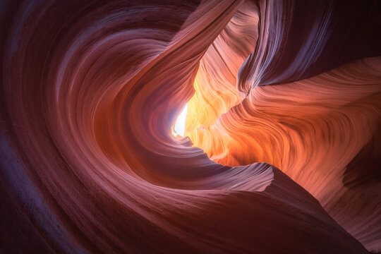 View of swirling sandstone walls, carved by time and water, glow with warm orange and purple hues in a slot canyon, Escalante, Utah, United States.