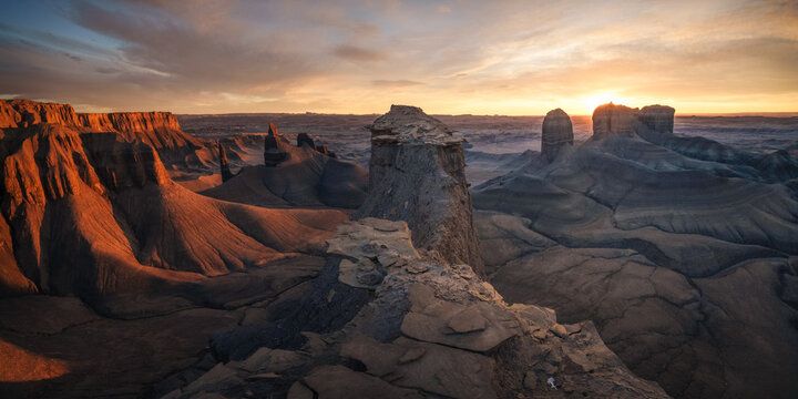 View of stark mesas and buttes bathed in the warm glow of the setting sun, casting long shadows across the arid landscape, Hanksville, Utah, United States.