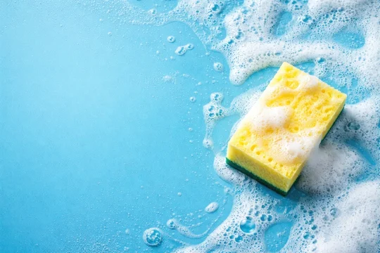Cleaning concept banner with a sponge and soap foam on blue background from top perspective including copy space