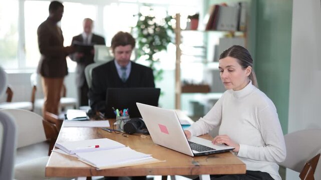 European woman sitting at desk is working on laptop computer. Working day in office of business structure, woman is working at computer. Regional representative office of international company 