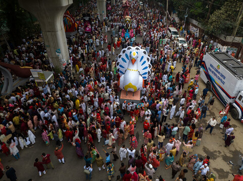 Dhaka, Bangladesh - 13 April 2026: Aerial view of a vibrant parade with a giant peacock float and dense crowds, framed by metro pillars.