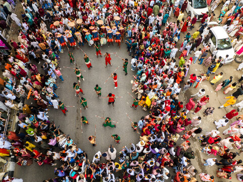 Dhaka, Bangladesh - 13 April 2026: Aerial view of a vibrant street performance, with red and green costumed figures amid a dense, colorful crowd on grey pavement.