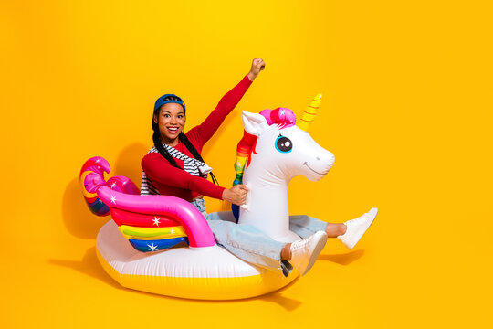 Young woman on a colorful inflatable unicorn rides in a bright yellow studio with a joyful pose