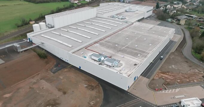 Low angle aerial track showing the side of a large modern white industrial facility with loading bays