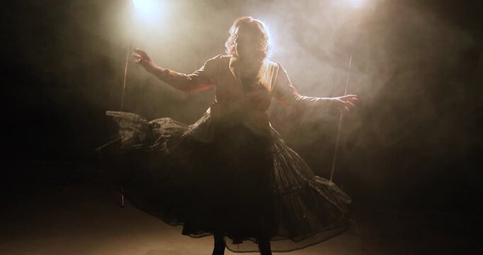A dancer performs in slow motion on a dark smoky stage, lifting a flowing skirt under bright backlights for a dramatic theatrical silhouette scene