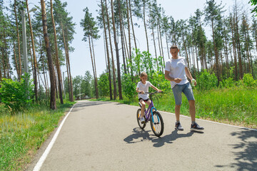 Naklejka premium Dad teaches daughter to ride a bike. Girl sat on bicycle for the first time, his father teaches child to ride a bicycle.