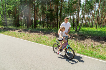 Obraz premium Father teaching his daughter how to ride a bicycle in forest