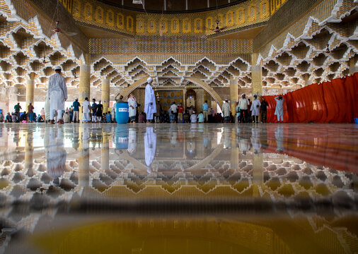 Tangail, Bangladesh - 21 March 2021: View of the grand mosque's interior, its golden, reflective floor mirroring intricate geometric walls as worshippers gather.