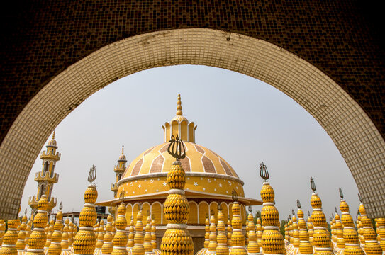 View of a golden dome and minarets rise majestically against the sky, framed by the intricate archway, in Tangail, Dhaka Division, Bangladesh.