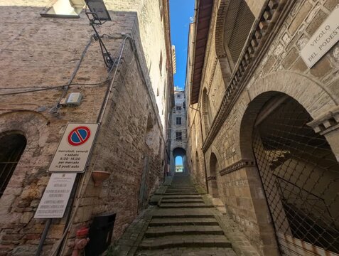 Vicolo stretto tra edifici storici in pietra, con archi, finestre e pavimentazione in ciottoli. Una scena suggestiva che cattura l&rsquo;atmosfera autentica di un borgo antico italiano