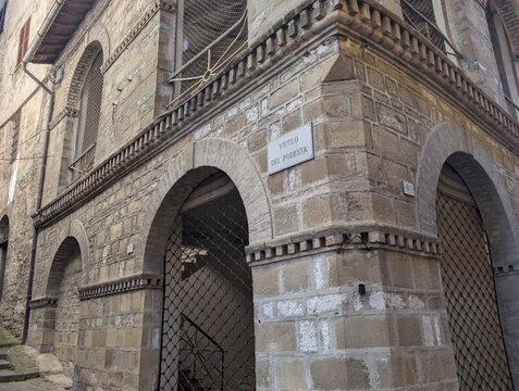 Edificio storico in pietra con archi e dettagli architettonici tradizionali lungo una via. Una scena urbana dal carattere antico che valorizza materiali, texture e atmosfera dei borghi italiani