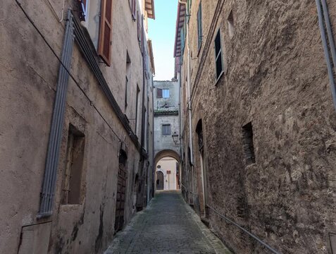 Vicolo stretto tra edifici storici in pietra, con archi, finestre e pavimentazione in ciottoli. Una scena suggestiva che cattura l&rsquo;atmosfera autentica di un borgo antico italiano