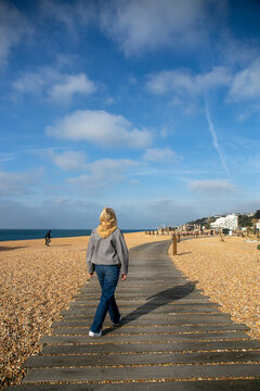 Woman walking along the boardwalk at Folkestone Beach in Kent, England, with pathways made from old railway sleepers across the pebbles. The scene captures the relaxed atmosphere of the seaside