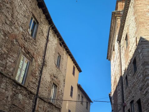Inquadratura dal basso di edifici storici in pietra illuminati dal sole, con cielo azzurro nitido. Una scena architettonica che valorizza texture antiche, luce naturale e atmosfera urbana tradizionale