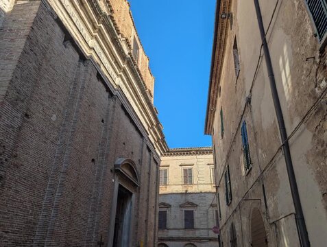 Inquadratura dal basso di edifici storici in pietra illuminati dal sole, con cielo azzurro nitido. Una scena architettonica che valorizza texture antiche, luce naturale e atmosfera urbana tradizionale