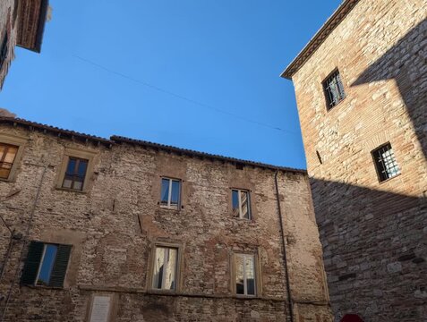 Inquadratura dal basso di edifici storici in pietra illuminati dal sole, con cielo azzurro nitido. Una scena architettonica che valorizza texture antiche, luce naturale e atmosfera urbana tradizionale