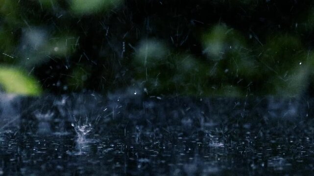 Heavy rain drops falling and splashing on dark wet surface during monsoon at night close-up