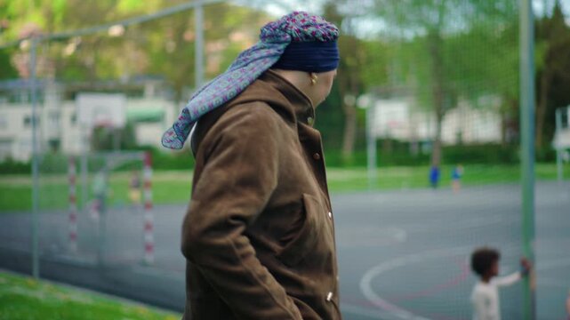 Cancer patient woman walking near school basketball court observing children expressing resilience recovery hope and everyday life during treatment in suburban setting