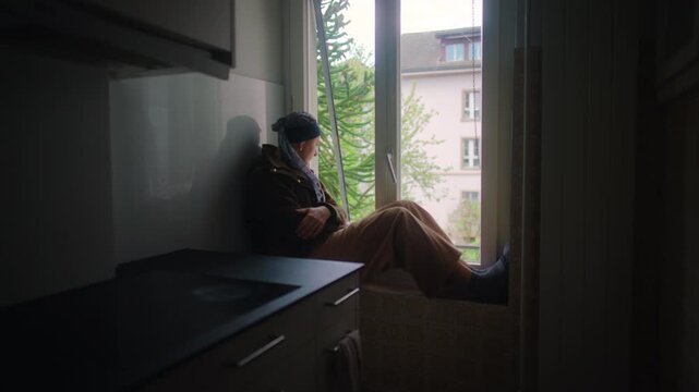 cancer patient resting at window in apartment kitchen coping with chemotherapy recovery isolation and emotional resilience during treatment journey at home reflecting on healing