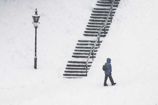View of a solitary figure ascending snow-covered steps next to a vintage lamppost in a serene winter scene, Tallinn, Estonia.