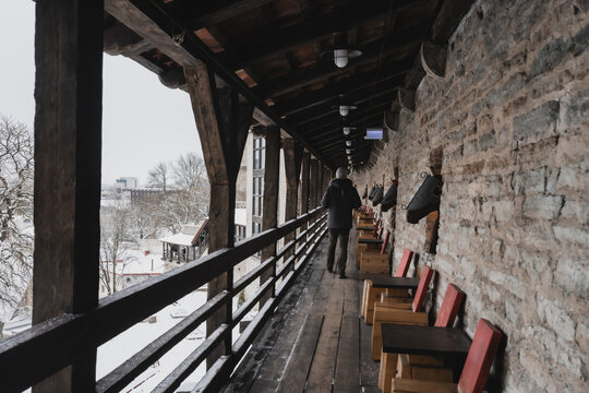 View of a solitary figure walking along a wooden parapet, the ancient stone wall contrasting with the modern city beyond, Tallinn, Estonia.