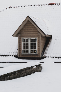 View of a snow-covered roof with a dormer window featuring white panes, a stark contrast against the muted tones of the surrounding building, Tallinn, Estonia.