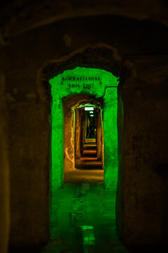 View of a long tunnel with green lights illuminating the damp walls and a glimpse of distant figures, casting shadows in Tallinn, Estonia.