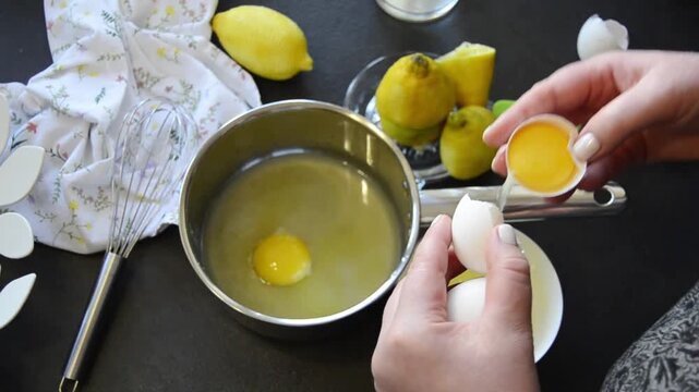 Close-up of hands cracking an egg into a bowl with visible yolk and egg white. Home cooking process with fresh ingredients and kitchen utensils on the table.
