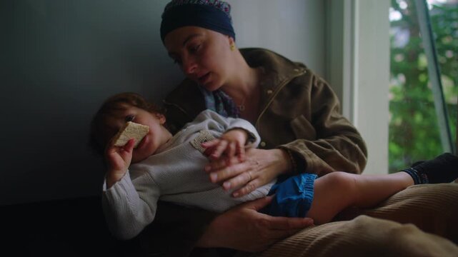 mother with cancer comforting child on lap at home window during chemotherapy treatment expressing nurturing care emotional support and resilience through illness recovery journey