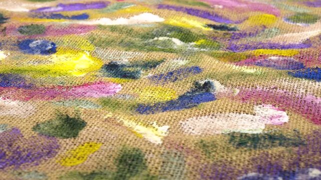Various multi-colored spots of different shapes from paint brushes with gouache and acrylic paint on the beige burlap fabric, abstract background, side view