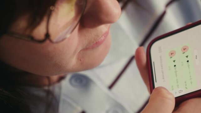 A close up focused on a womans face as she smiles and dictates a message into her phone. She is wearing glasses and speaking to the messaging app capturing a relaxed and natural moment of voice typing