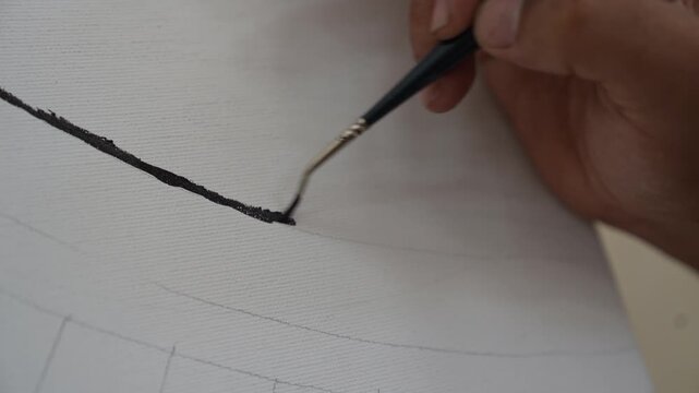 A high-definition macro shot focusing on the tip of a fine-detail paintbrush as it applies a smooth black line to a textured white canvas. The artist follows faint pencil sketches, high precision