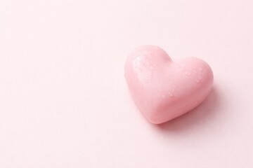 Fototapeta premium Heart shaped pink soap on a pale pink flat panel background with ample copy space