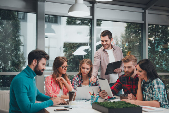 Young creative team of colleagues collaborating around laptops and tablet during an informal office meeting and brainstorming session