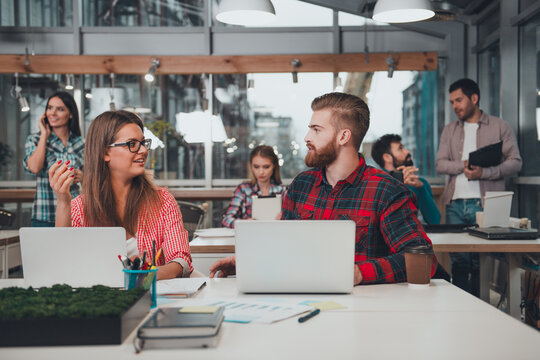 Young coworkers collaborating in a modern open office workspace, casual team meeting with laptops and coffee, creative startup environment and friendly conversation