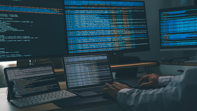 Man using AI chatbot while coding at a multi monitor workstation with laptop and screens displaying scripts, showing software development, automation workflow, and programming productivity in office s