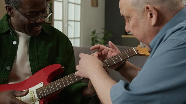 Close up shot of senior African American man learning to play electric guitar and smiling with music teacher correcting hand position Great for progress tracking or skill development platforms