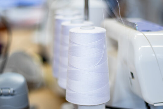 White sewing thread spools arranged neatly beside a sewing machine on a wooden table in a sewing cafe, showcasing tools and materials for textile projects