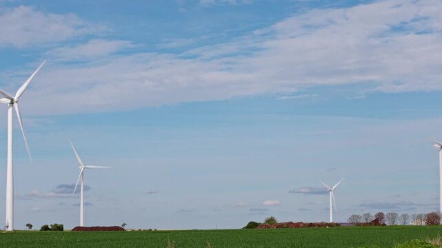Alternative energy sources. Large wind turbines with blades rotate in wind in green agricultural wheat and colza fields aerial view cloudy sky