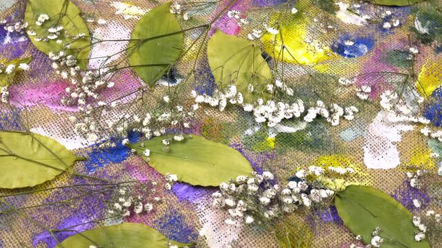 Flat dried flower arrangements. Dried pressed gypsophila paniculata    flowers and camellia leaves lie on the beige burlap cloth with abstract painting, background, top view 