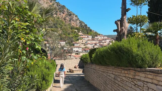 Woman tourist walk sightseeing old Gorica quarter residential district in Berat. Tiered Ottoman narrow old cobblestone streets in sunny summer day in Albania