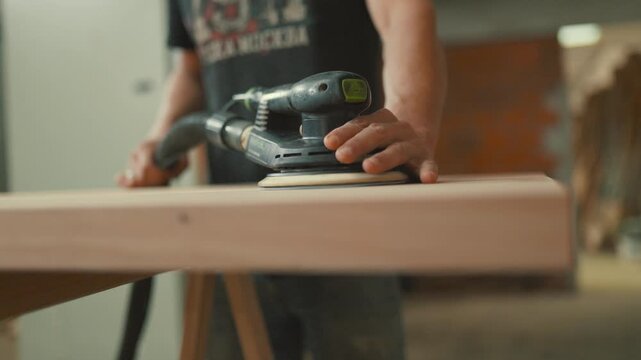 Carpenter using orbital sander on wood plank