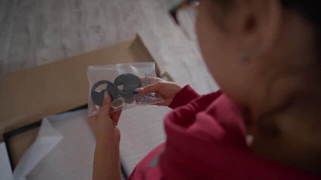Woman Assembling Furniture Examining Caster Wheels And Small Fittings, Plastic Bag Of Wheels In Hands, Bright Floorwork Scene, Planning Placement And Orientation Before Installation