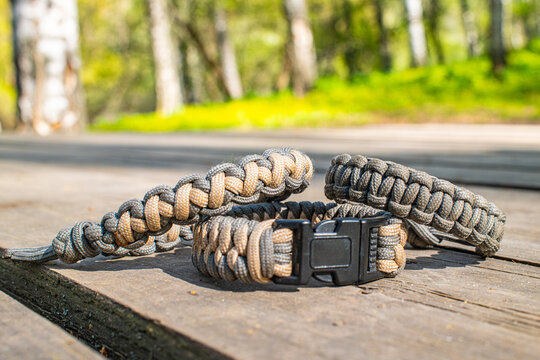 Handmade paracord survival bracelet with buckle on rustic wooden table in forest, outdoor camping adventure gear