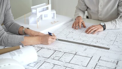 Obraz premium Architects discussing new construction project plans, working on blueprints with a contemporary house model, collaborating on urban design and future development, close up