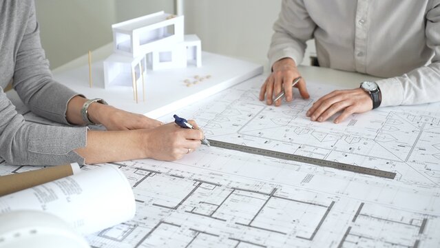 Architects discussing new construction project plans, working on blueprints with a contemporary house model, collaborating on urban design and future development, close up