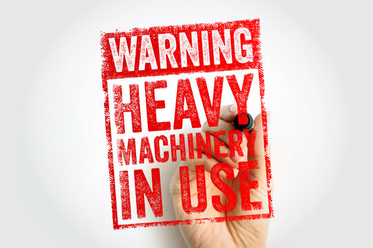 WARNING HEAVY MACHINERY IN USE text on stamp. Safety alert for industrial equipment operation and mechanical hazards in factory. Hand holding marker with important workplace machinery notice