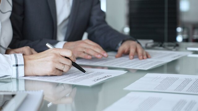 Group of professional business people sitting at a meeting table, reading and discussing contract terms, financial agreements. Collaboration, teamwork, and corporate communication concept