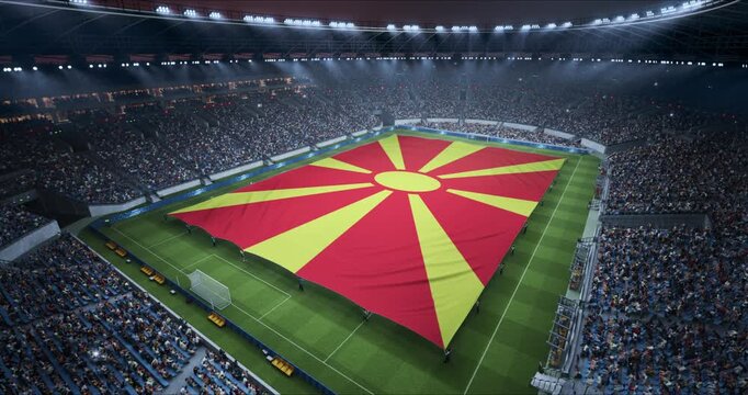 Professional Stadium Soccer Game Championship With Flag of North Macedonia Spread Across the Pitch Before Football Match Start. Cheering Crowds of Fans Surround the Field. Aerial Elevated Static Shot