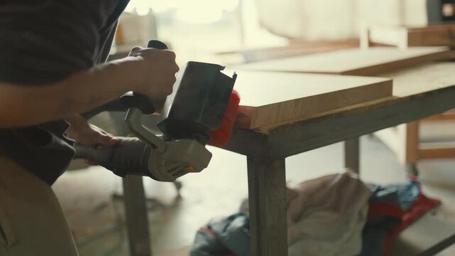 Carpenter using an electric brush sander on a wooden board